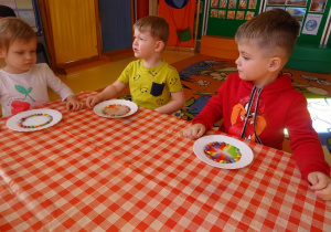 Troje dzieci obserwuje jak rozpuszczają się cukierki w wodzie na talerzykach.